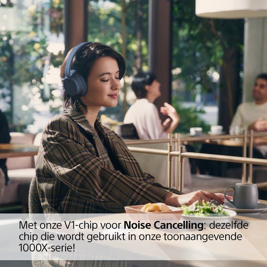Een vrouw met een blauwe Sony WH-CH720N koptelefoon in een café.