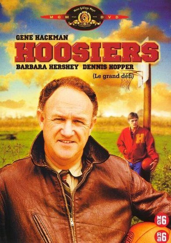 Gene Hackman met een bruine jas en stropdas, met op de achtergrond een jongen met een basketbal.
