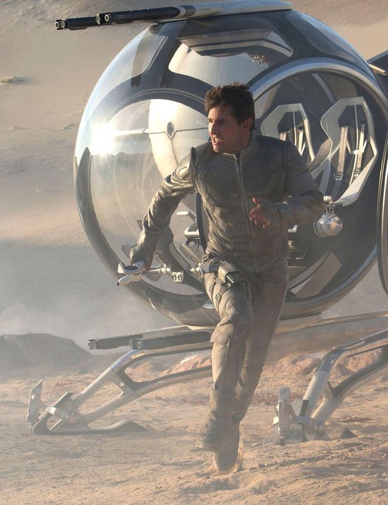Tom Cruise in grijs pak met wapen, rent weg van een buitenaards voertuig.