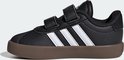 Zijaanzicht van zwarte Adidas sneakers met witte strepen en klittenbandsluiting op bruine zool.
