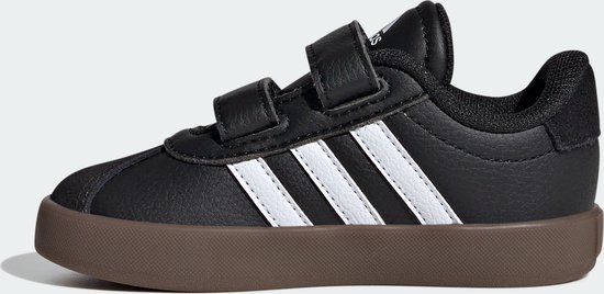 Zijaanzicht van zwarte Adidas sneakers met witte strepen en klittenbandsluiting op bruine zool.