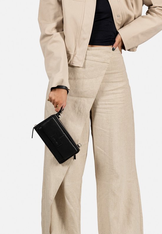 Zwarte telefoonportemonnee met croco-look, gedragen door een model met beige jasje en wijde linnen broek.