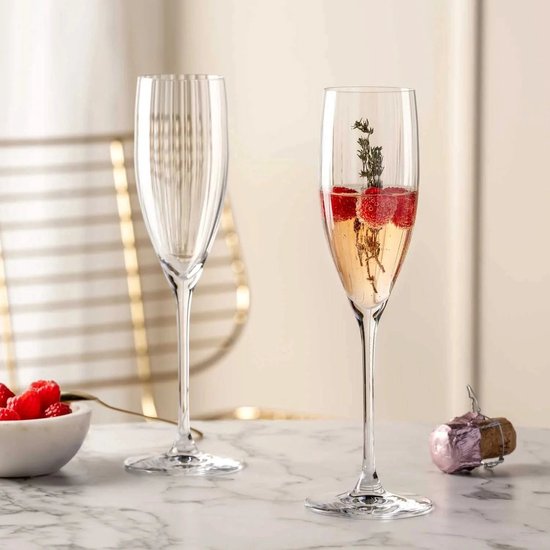 Twee champagneglazen met verticale ribbels. Eén glas bevat champagne met frambozen en takjes.