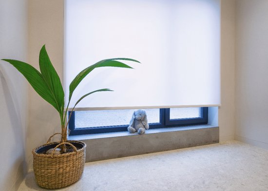 Witte rolgordijn boven een raam met een plantje en een konijntje op de vensterbank.