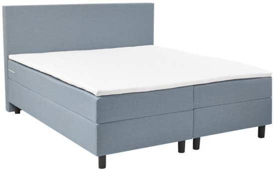 Blauwgrijze boxspring met hoofdbord en witte topper.