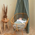 Baby slaapt in een rotan wieg met groen-witte stippen deken, gedrapeerd met een groene sluier.