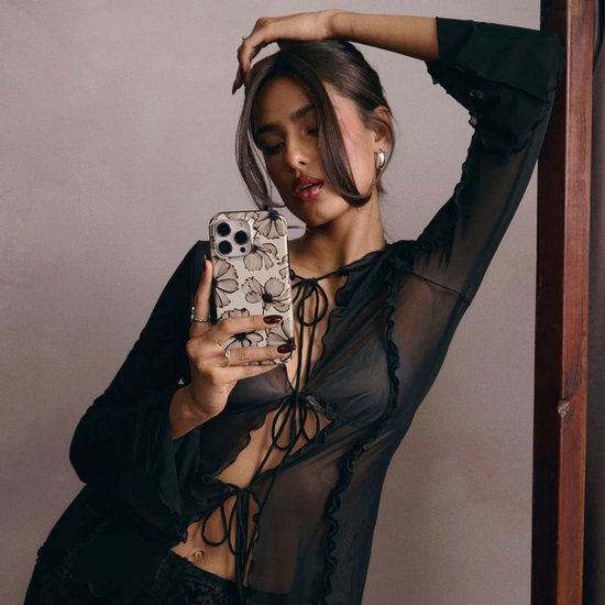 Model met telefoonhoes met beige achtergrond en bloemenprint, maakt selfie.