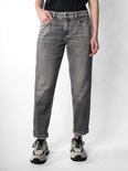Model draagt een grijze jeans met opgerolde broekspijpen en beige sneakers.