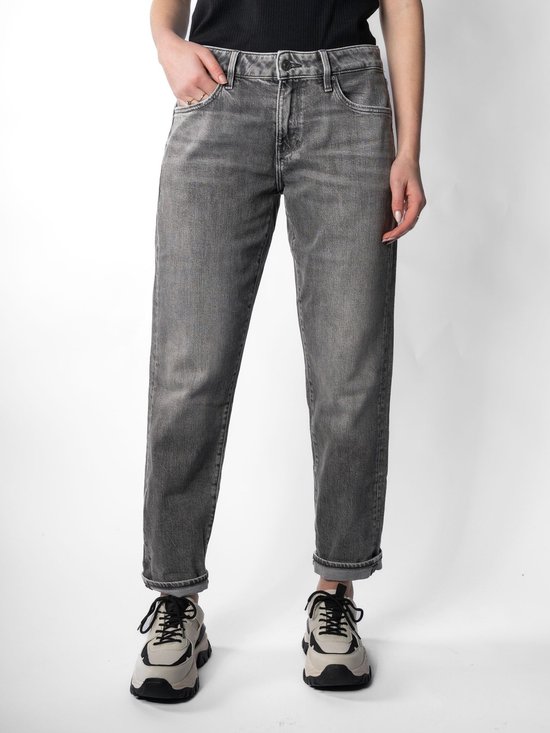 Model draagt een grijze jeans met opgerolde broekspijpen en beige sneakers.