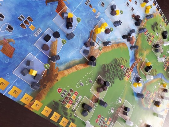 Detail van een bordspel met water, groen land en vele houten spelcomponenten.