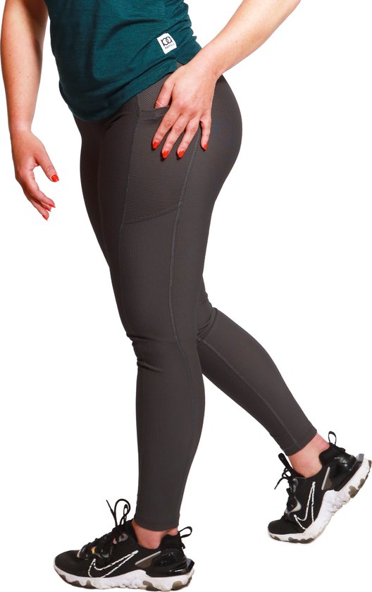 Model met grijze ribbel sportlegging met hoge taille, zakken en zwarte sneakers, met een groen shirt.
