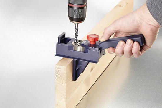 Blauwe deuvelmal met rode knop, die door een hand wordt vastgehouden om een gat te boren in een houten balk.