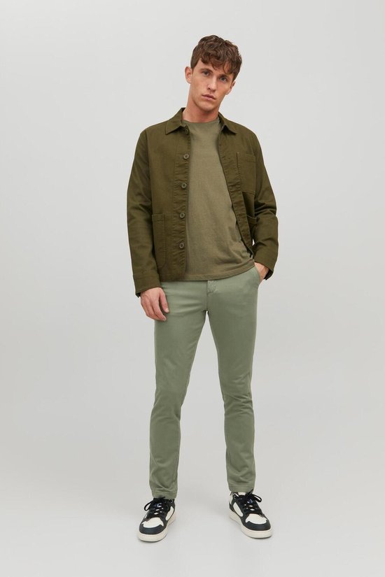 Man staat met smalle, lichtgroene broek en groen jack.