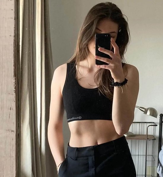 Jong model neemt spiegel selfie in zwarte nauwsluitende crop top en zwarte broek.