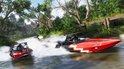 Twee raceboten, één rood met witte zigzag, varen snel over een rivier door een groen bosrijk gebied.