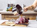 Hand giet vloeistof uit een RVS steelpan in een pot met rode ui