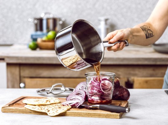 Hand giet vloeistof uit een RVS steelpan in een pot met rode ui