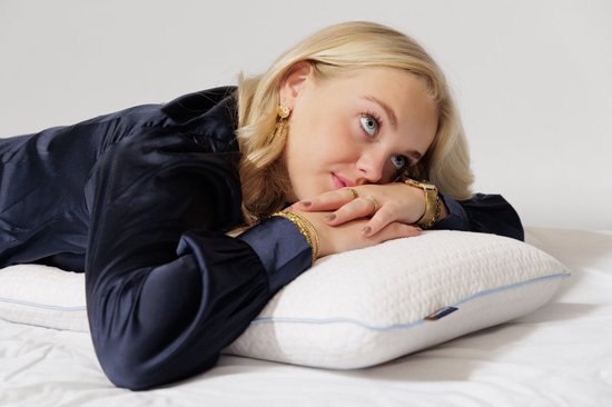 Blond meisje met een donkerblauwe satijnen blouse die op een wit kussen leunt.