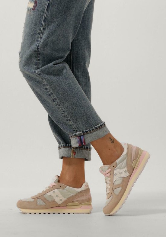 Dames met beige Saucony sneakers aan, met roze veters en jeans.