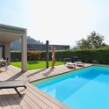 Vrouw in bikini neemt een douche bij een zwembad met de zwarte AREBOS buitendouche. Omringd door een terras en groen.