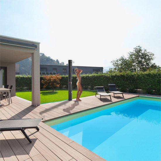 Vrouw in bikini neemt een douche bij een zwembad met de zwarte AREBOS buitendouche. Omringd door een terras en groen.