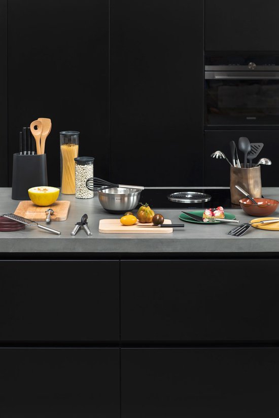 Plan de travail de cuisine avec divers ustensiles, dont un couteau économe, des spatules, un fouet et une râpe.