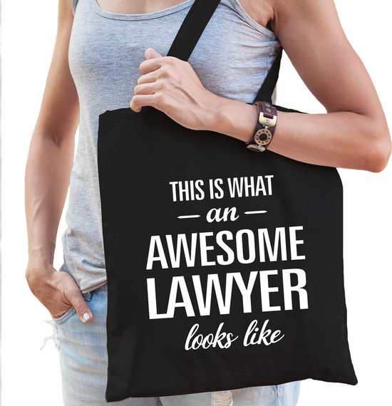 Sac noir avec inscription blanche "This is what an awesome lawyer looks like". Porté par une femme avec un haut gris et un jean.
