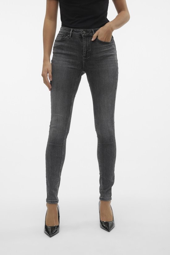 Vrouw in zwarte top en grijze Vero Moda skinny jeans, staand.
