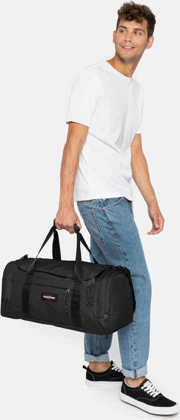 Man met spijkerbroek draagt een zwarte Eastpak Reader S+ reistas.