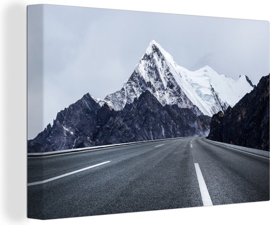 Canvas Schilderij Zwart-wit foto van een weg door besneeuwde bergtoppen - 180x120 cm - Wanddecoratie XXL
