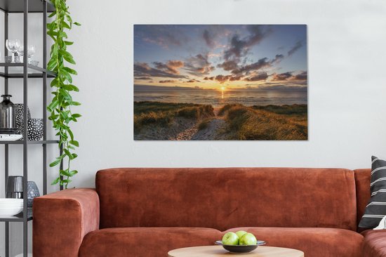 Chambre avec un canapé orange-brun et sur le mur une toile d'un coucher de soleil sur les dunes.