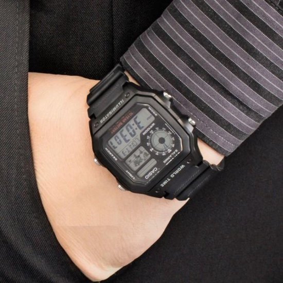 Zwarte Casio World Time horloge gedragen op een pols met gestreepte mouw.