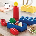 Rode LEGO fles met LEGO hoofd, blauwe en rode LEGO lunchboxen. Gele LEGO stenen op een tafel.