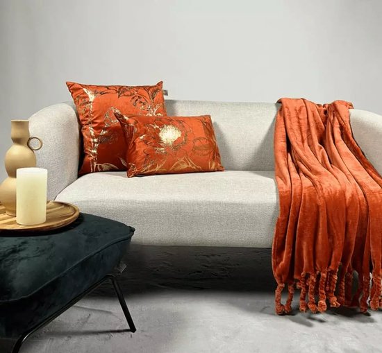 Bank met twee oranje kussens met gouden bloemenprint en een oranje plaid met flosjes.