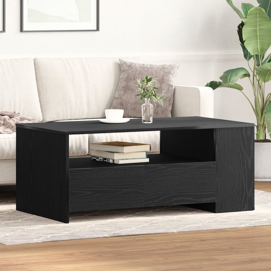 Table basse noire à grain de bois, dans un salon avec canapé et plante.