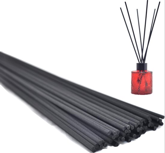 Stapel donkere geurstokjes naast een kleine rode diffuserfles met zwarte stokjes.