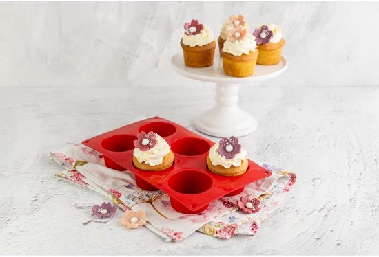Twee rode siliconen muffinvormen, één met drie gedecoreerde cupcakes met witte crème en bloemen.