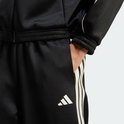 Detail van een zwarte trainingsbroek met beige 3-strepen en adidas logo op de zak.