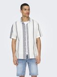 Man in wit kort overhemd met verticale grijze strepen en jeansshort.