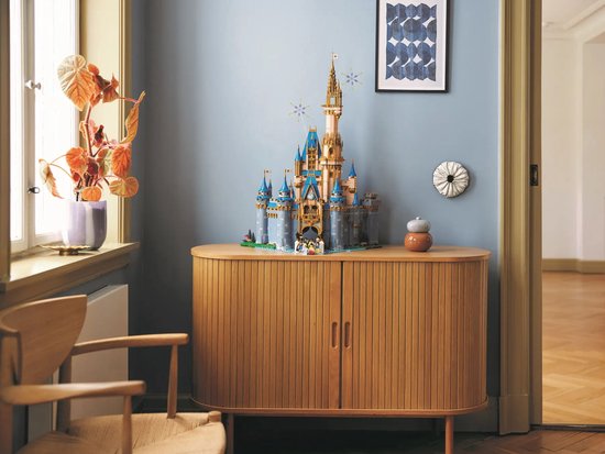 Het LEGO Disney Kasteel staat op een houten kast, in een woonkamer met blauwe muren.