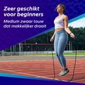 Vrouw met blauwe legging en witte top die op een atletiekbaan springtouwt.