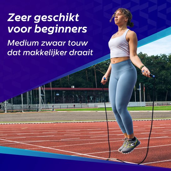 Vrouw met blauwe legging en witte top die op een atletiekbaan springtouwt.