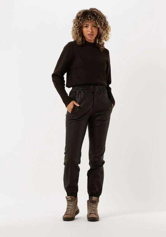 Model met krullend haar draagt een donkerbruine leren broek met elastische tailleband en een bijpassende trui.