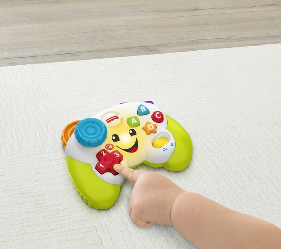Een kindervingertje drukt op de rode '2'-knop van een Fisher-Price controller. Het speelgoed is wit met groene handvatten, een lachend gezicht en ABC-knoppen.