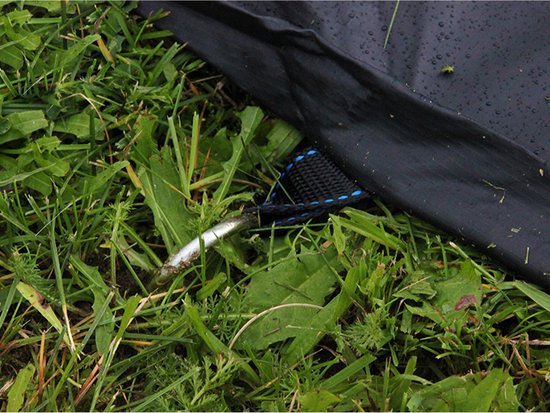 Zwarte trampoline afdekhoes met bevestigingslus op gras.