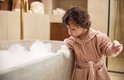 Peignoir rose à capuche, porté par un enfant près d'une baignoire.
