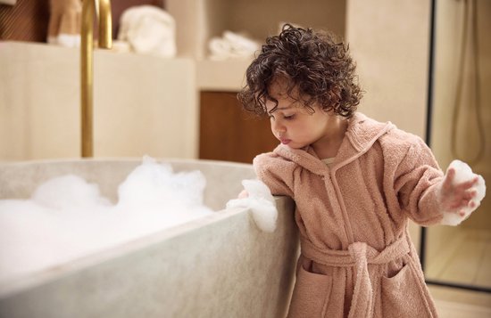 Peignoir rose à capuche, porté par un enfant près d'une baignoire.