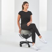 Vrouw met paardenstaart zit op een grijs-zwarte balstoel, in een zwarte top en legging, met witte sneakers.