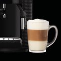 Zwarte Krups espressomachine met een glas latte macchiato met drie lagen, naast de machine.