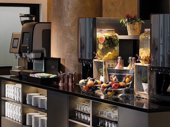 Een buffet met diverse drankdispensers, fruit en gebak, met een koffiezetapparaat in de linkerbovenhoek.
